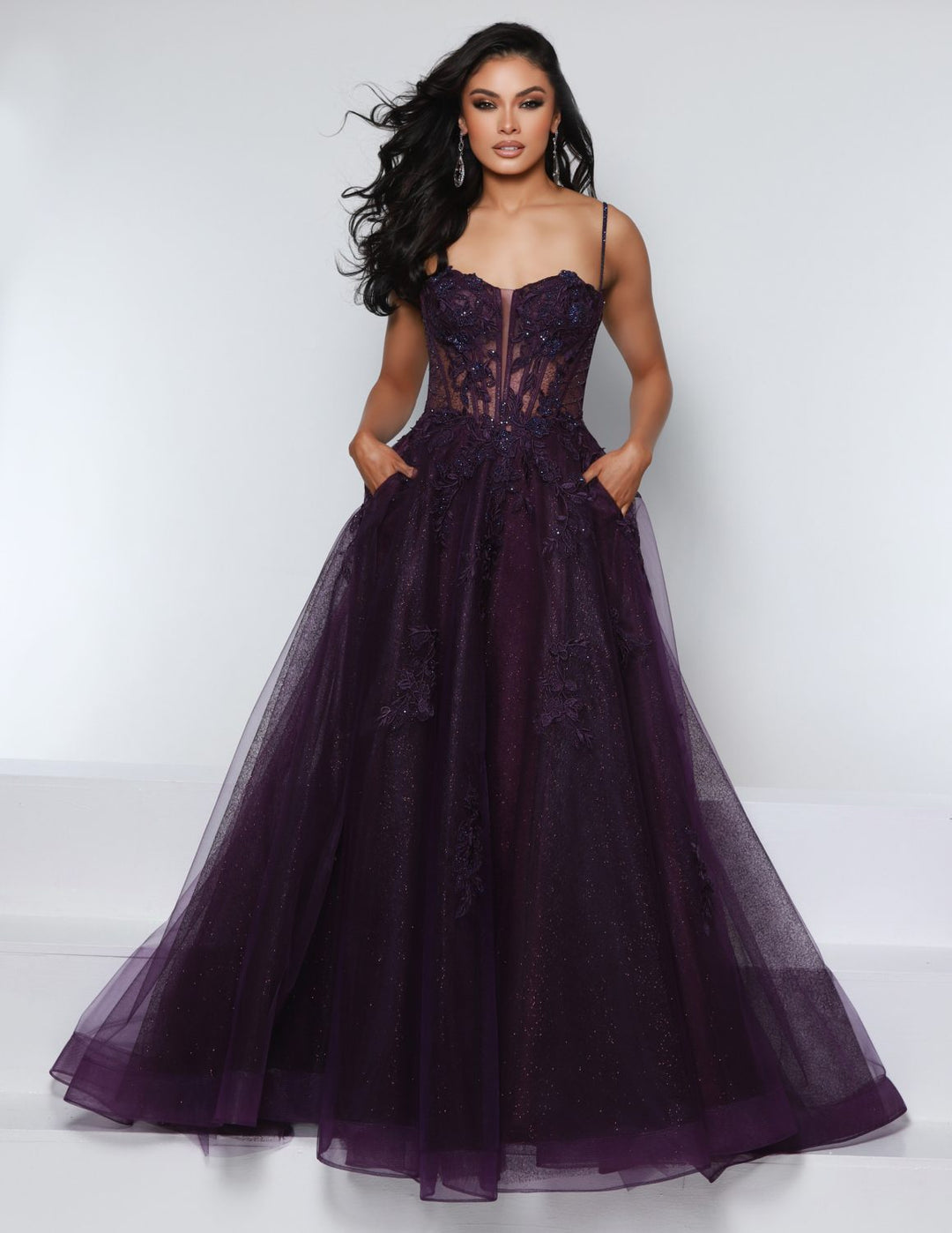 A woman wears the 2Cute 25932 by 2Cute—a dark purple, floor-length fitted ball gown with a sheer bodice and floral lace details—standing before a plain light background.