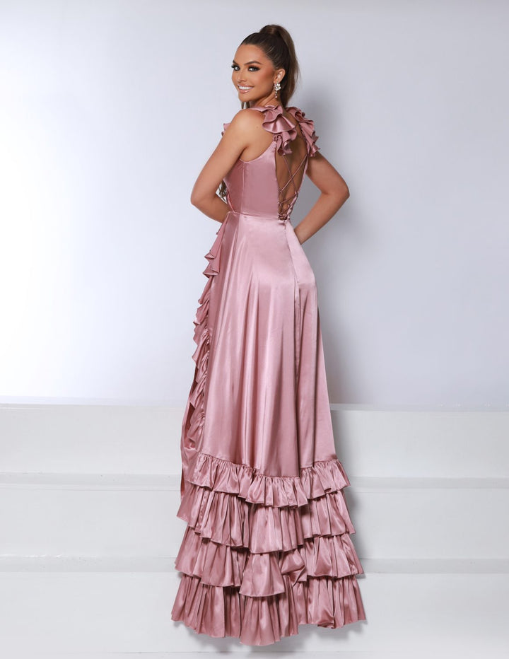 Wearing the 2Cute 25380 by 2Cute, a woman in a shiny, pink, floor-length gown with ruffled layers and an open lace-up back smiles over her shoulder while standing on white steps.