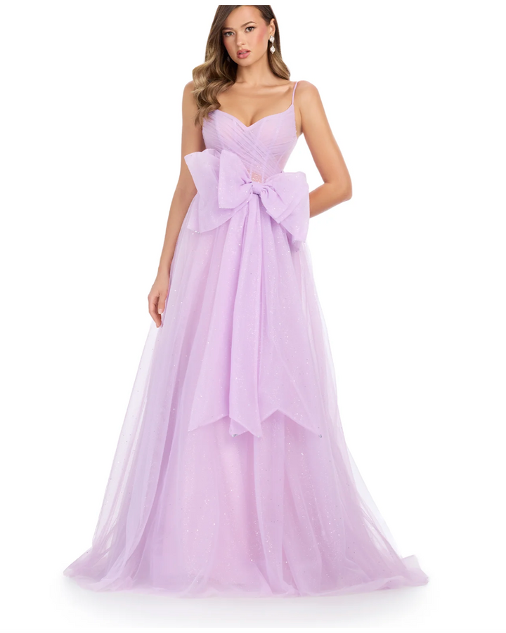 Wearing the Ashley Lauren 11841 by Ashley Lauren, a woman stuns in a light purple floor-length gown featuring thin straps, a sweetheart neckline, bow waist accent, and a glitter tulle skirt for subtle sparkle.